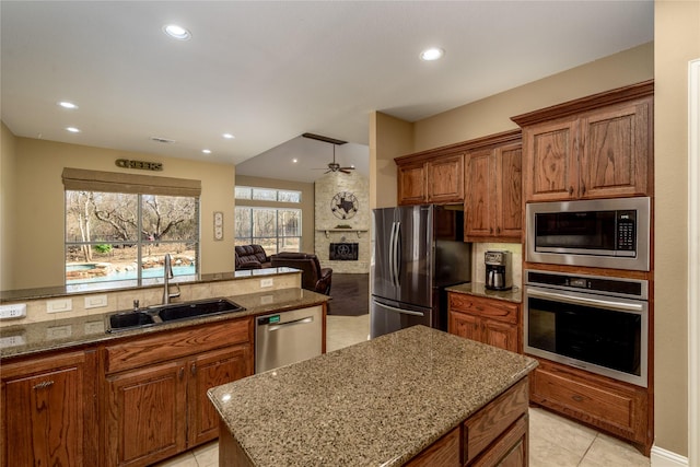 kitchen featuring ceiling fan, stone counters, brown cabinets, appliances with stainless steel finishes, and a sink