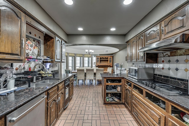 kitchen with brick floor, under cabinet range hood, a sink, appliances with stainless steel finishes, and an inviting chandelier