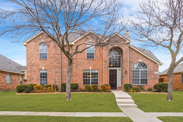 view of front of home featuring brick siding, a chimney, and a front yard