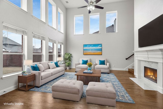 living room with a fireplace, dark wood-type flooring, a ceiling fan, baseboards, and stairs