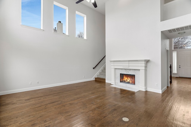 unfurnished living room featuring visible vents, dark wood finished floors, a towering ceiling, ceiling fan, and a high end fireplace