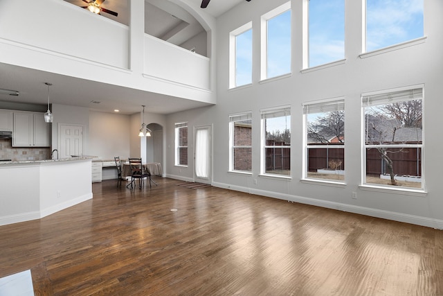 unfurnished living room with dark wood-style floors, ceiling fan, a sink, and baseboards