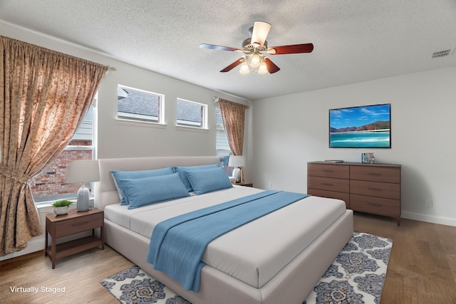 bedroom with visible vents, a ceiling fan, a textured ceiling, wood finished floors, and baseboards