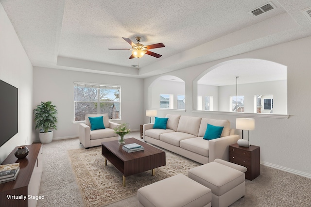 living room featuring a raised ceiling, visible vents, light carpet, a textured ceiling, and baseboards