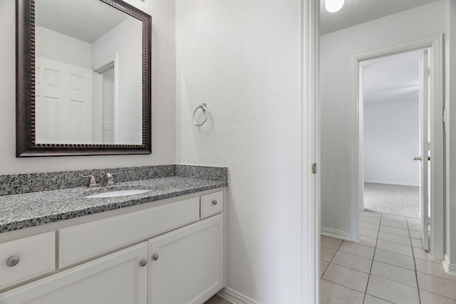 bathroom featuring a textured ceiling, a textured wall, tile patterned flooring, vanity, and baseboards