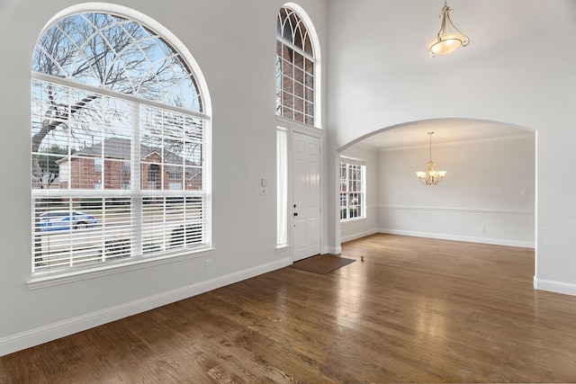 entrance foyer featuring baseboards, arched walkways, dark wood-type flooring, a high ceiling, and a notable chandelier