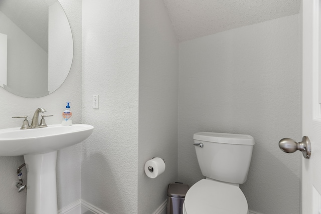 bathroom with a sink, a textured wall, a textured ceiling, and toilet