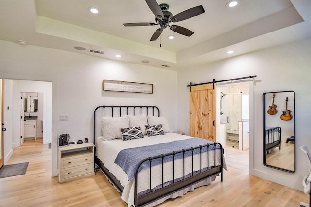 bedroom with a tray ceiling, a barn door, light wood-type flooring, and visible vents