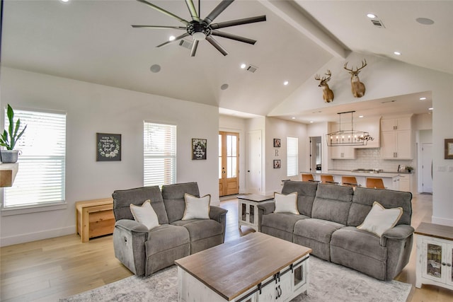 living area with a healthy amount of sunlight, light wood-type flooring, visible vents, and beamed ceiling