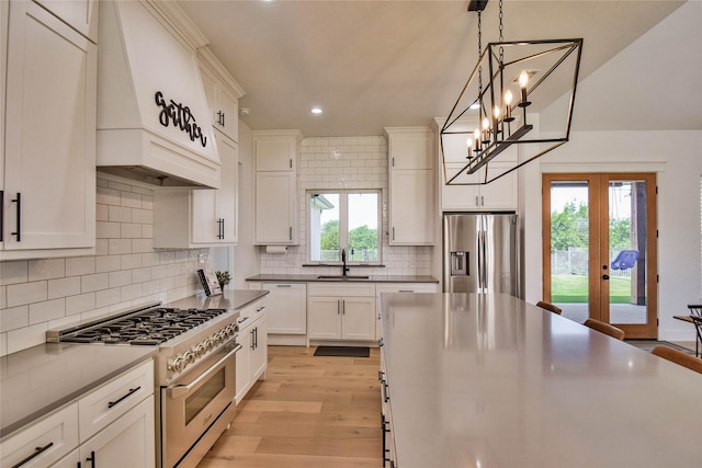 kitchen with light wood finished floors, appliances with stainless steel finishes, a sink, pendant lighting, and backsplash