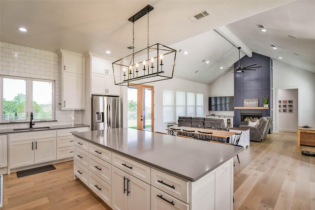 kitchen featuring a center island, stainless steel refrigerator with ice dispenser, dark countertops, open floor plan, and white cabinetry