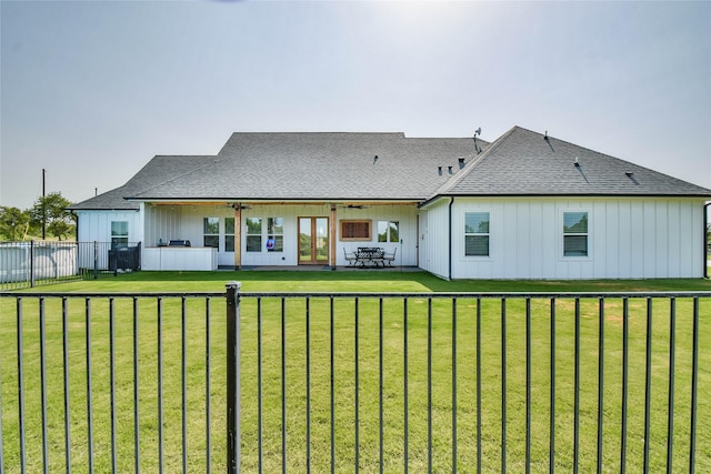 rear view of property featuring board and batten siding, a fenced backyard, a lawn, and roof with shingles