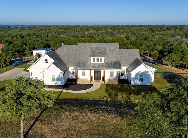 view of front of property with roof with shingles, a view of trees, and a front yard