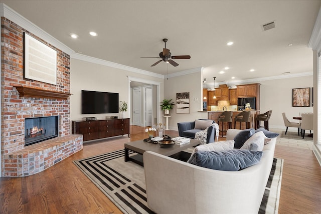 living area featuring light wood-style floors, visible vents, a fireplace, and crown molding