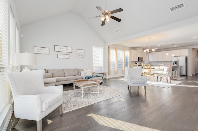 living area with dark wood-style floors, visible vents, high vaulted ceiling, and ceiling fan with notable chandelier