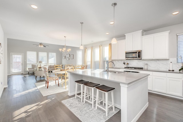 kitchen with a kitchen island with sink, white cabinets, stainless steel microwave, and a sink