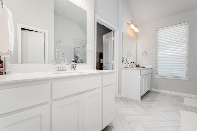 bathroom with baseboards, lofted ceiling, a sink, a walk in shower, and two vanities