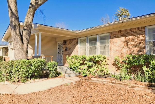 property entrance with a garage, covered porch, and brick siding