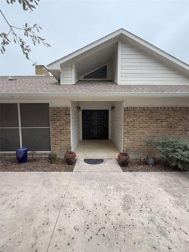 entrance to property featuring a shingled roof and brick siding