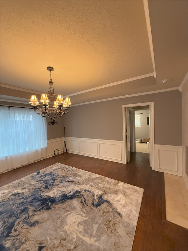 spare room featuring dark wood-style flooring, crown molding, a raised ceiling, wainscoting, and a chandelier