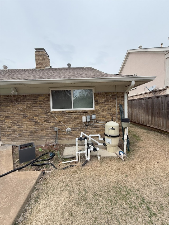 back of property with a chimney, roof with shingles, fence, a patio area, and brick siding