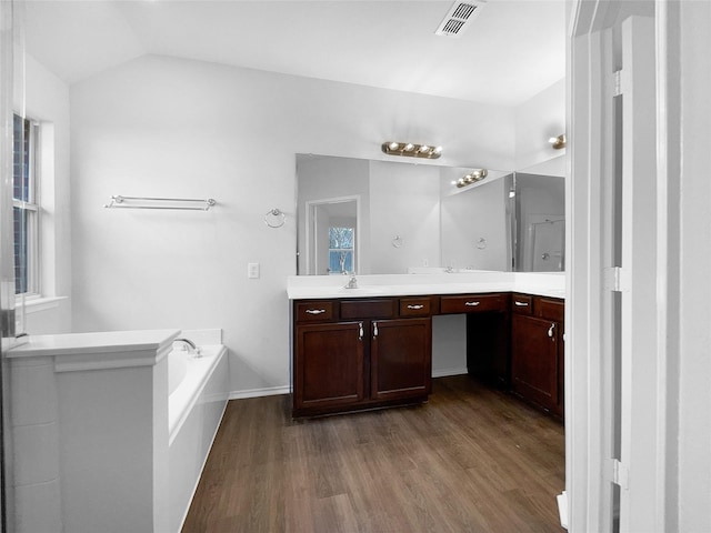 full bath featuring double vanity, visible vents, lofted ceiling, wood finished floors, and a garden tub