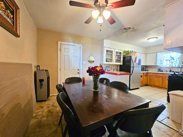 dining area with light tile patterned floors, a ceiling fan, visible vents, and a textured ceiling