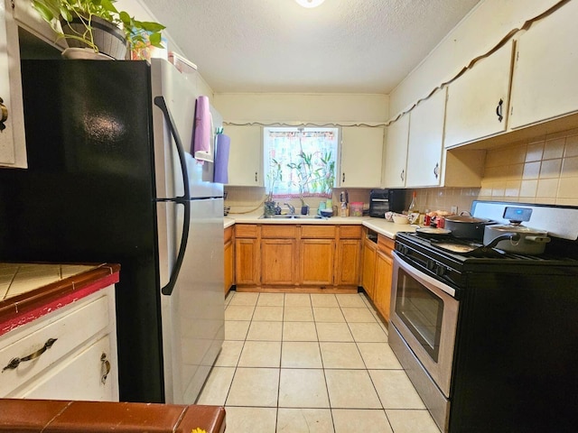 kitchen with stainless steel appliances, brown cabinetry, white cabinets, a sink, and light tile patterned flooring