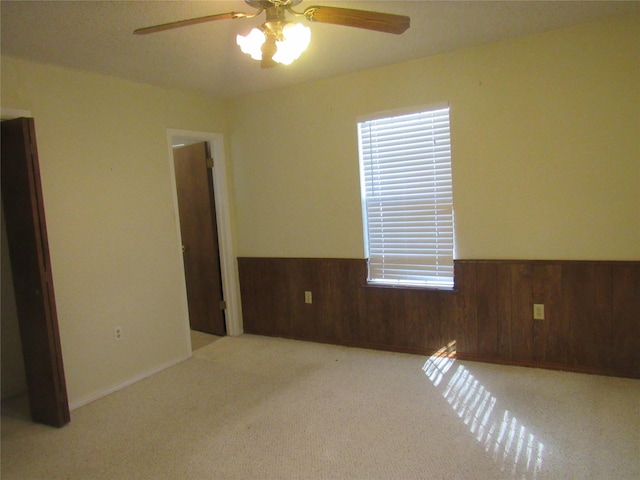 unfurnished room featuring a wainscoted wall, wood walls, light carpet, and ceiling fan