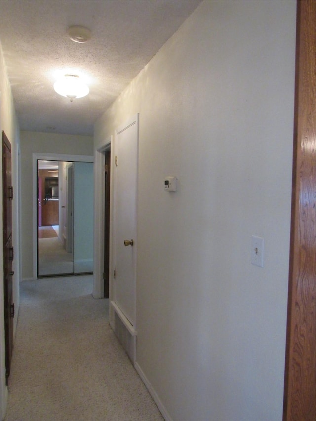 hallway with light colored carpet and a textured ceiling