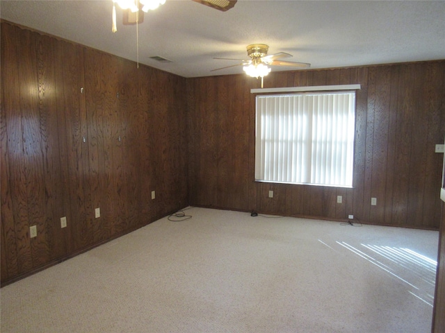 spare room featuring carpet floors, wooden walls, visible vents, and a ceiling fan