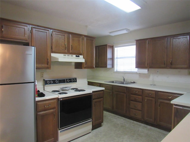 kitchen with under cabinet range hood, a sink, electric stove, light countertops, and freestanding refrigerator