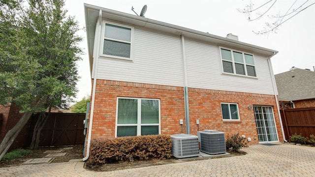 back of property featuring central AC, brick siding, a chimney, and fence