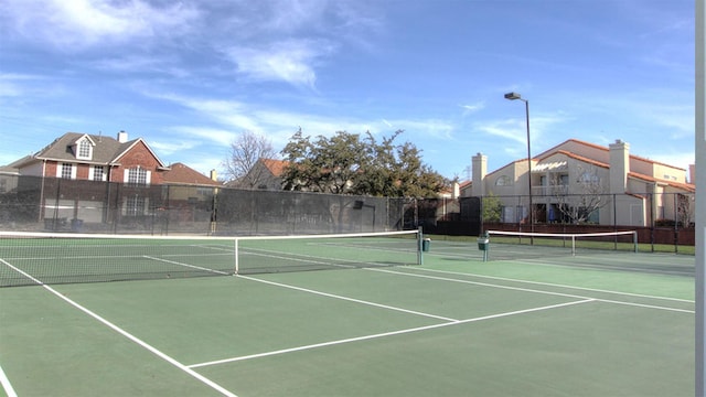 view of tennis court with a residential view and fence