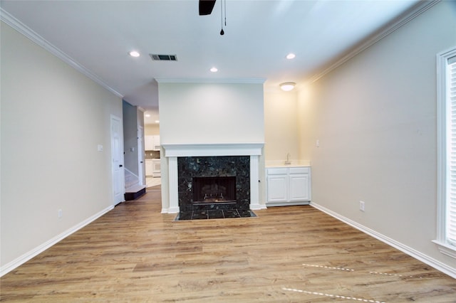 unfurnished living room featuring a fireplace, light wood finished floors, visible vents, ornamental molding, and baseboards