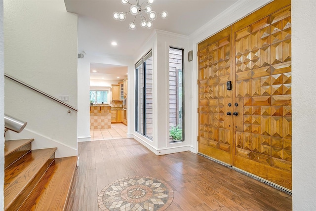 foyer entrance with stairs, a chandelier, wood finished floors, and crown molding