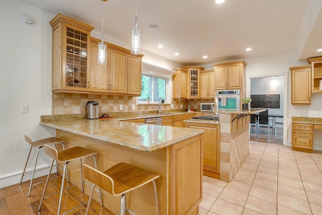 kitchen featuring a breakfast bar area, stainless steel appliances, hanging light fixtures, glass insert cabinets, and a peninsula