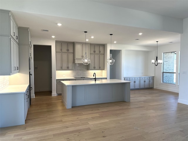 kitchen with light countertops, hanging light fixtures, an island with sink, and gray cabinets