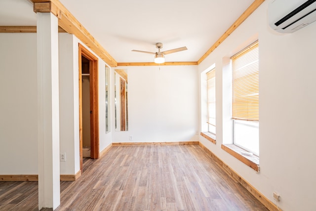 spare room with a wall unit AC, ceiling fan, baseboards, and wood finished floors