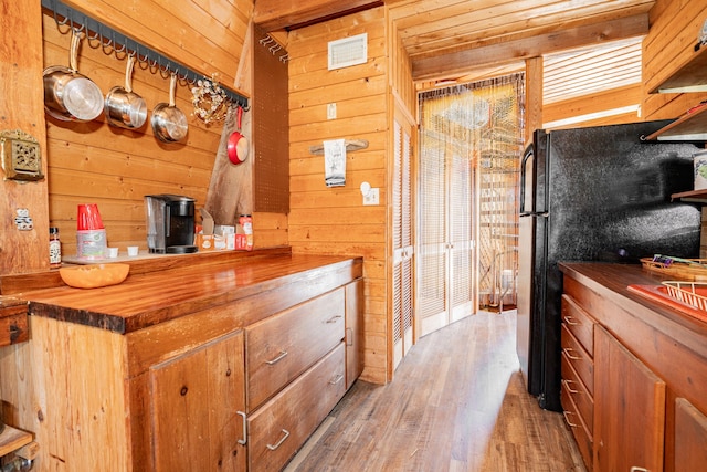 kitchen with brown cabinetry, butcher block counters, wood finished floors, freestanding refrigerator, and wood walls