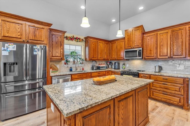 kitchen featuring stainless steel appliances, a sink, a center island, light stone countertops, and decorative light fixtures