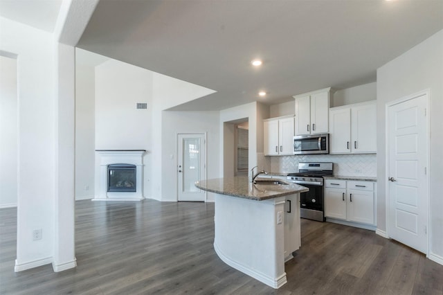 kitchen featuring a sink, white cabinets, appliances with stainless steel finishes, dark stone countertops, and a center island with sink