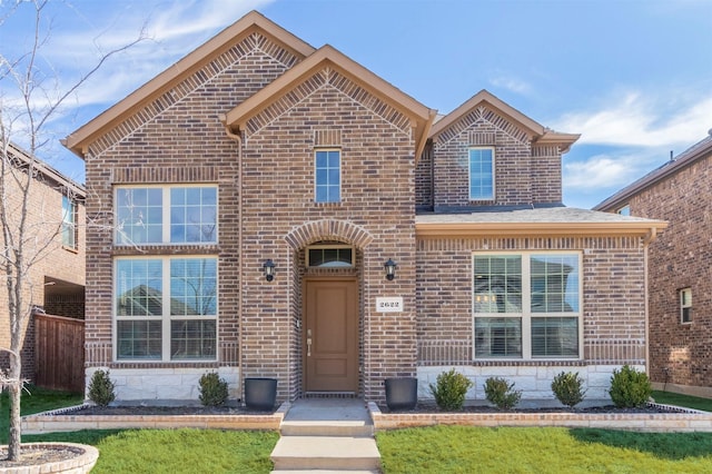 traditional-style home featuring stone siding, roof with shingles, a front yard, and brick siding