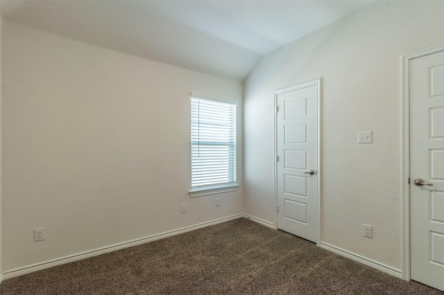 spare room with lofted ceiling, dark carpet, and baseboards