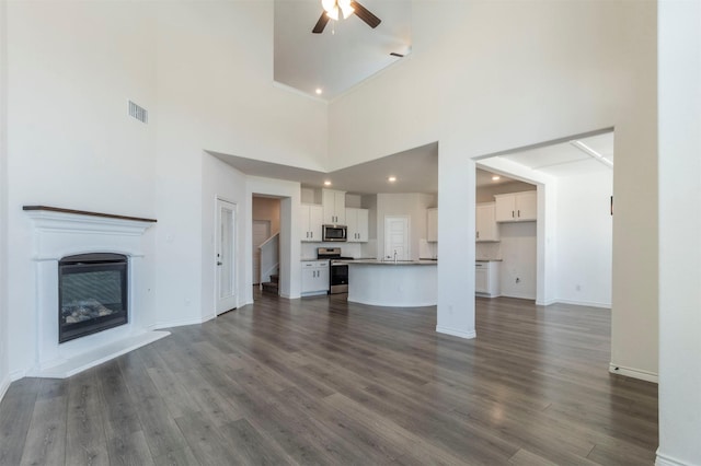 unfurnished living room with dark wood-style flooring, visible vents, a ceiling fan, a glass covered fireplace, and baseboards