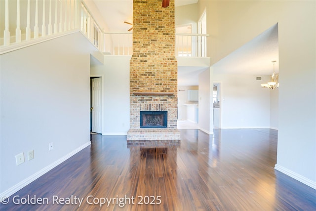 unfurnished living room featuring a brick fireplace, baseboards, and dark wood-type flooring