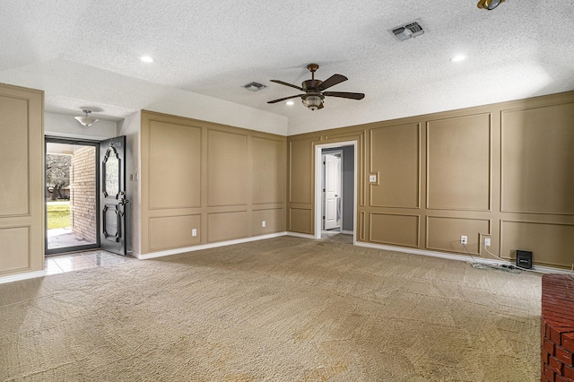 spare room featuring visible vents, a textured ceiling, light colored carpet, and a decorative wall