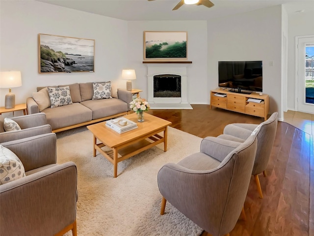 living room featuring a fireplace with raised hearth, wood finished floors, and a ceiling fan