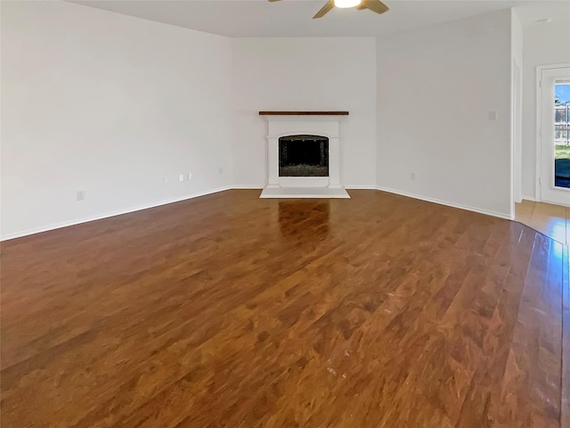 unfurnished living room featuring a fireplace with raised hearth, ceiling fan, dark wood-style flooring, and baseboards