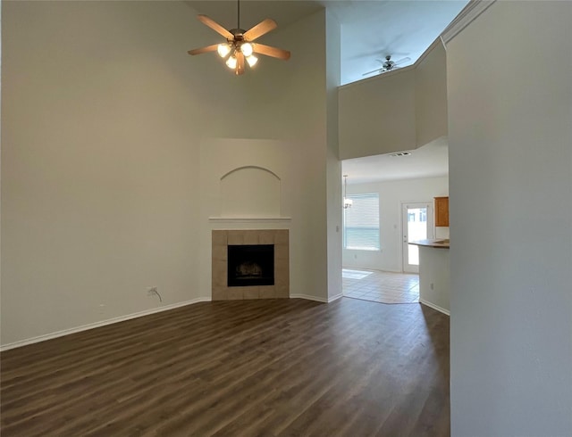 unfurnished living room with baseboards, a tile fireplace, ceiling fan, dark wood-type flooring, and a high ceiling